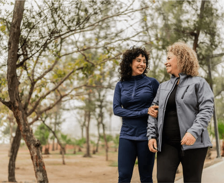 Two women walking arm in arm under trees