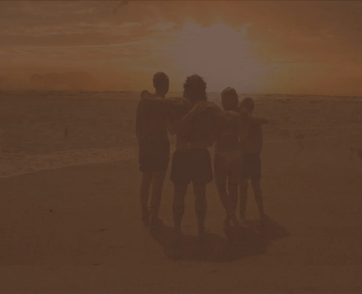 A family of four standing arm in arm on a beach at sunset
