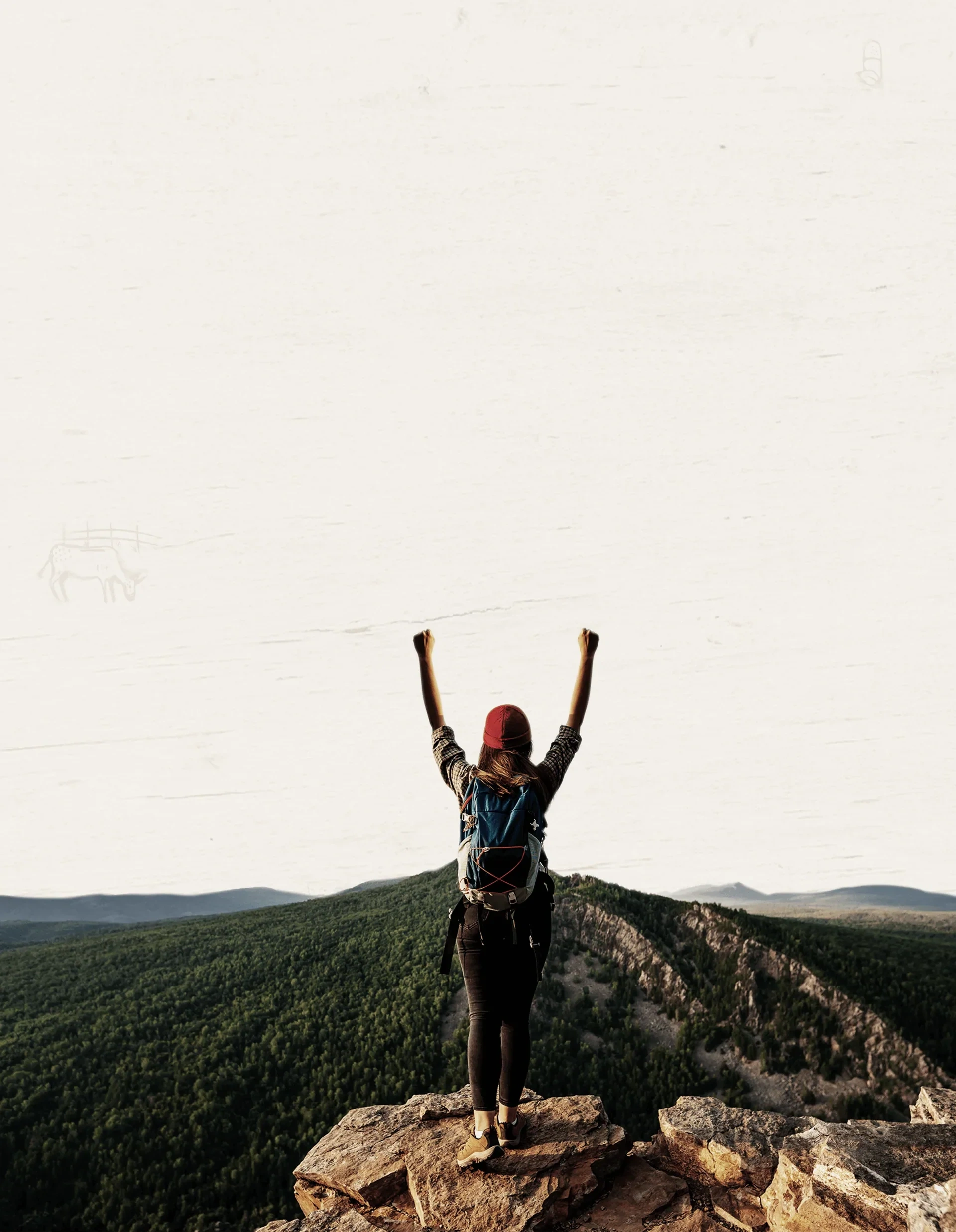 A hiker with both arms raised on a rock above a forested valley