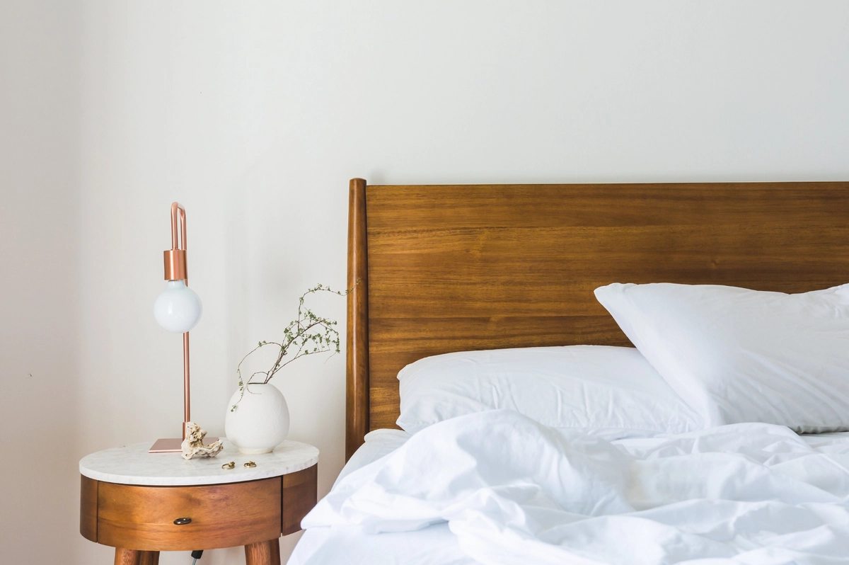 An unmade bed with white linen beside a wooden headboard